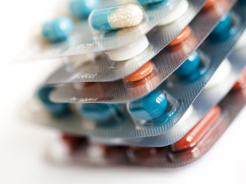 Foto mostra seis cartelas de remédios empilhadas, com comprimidos nas cores branca, laranja e azul e cápsulas metade azul e metade transparente com pequenas bolinhas dentro